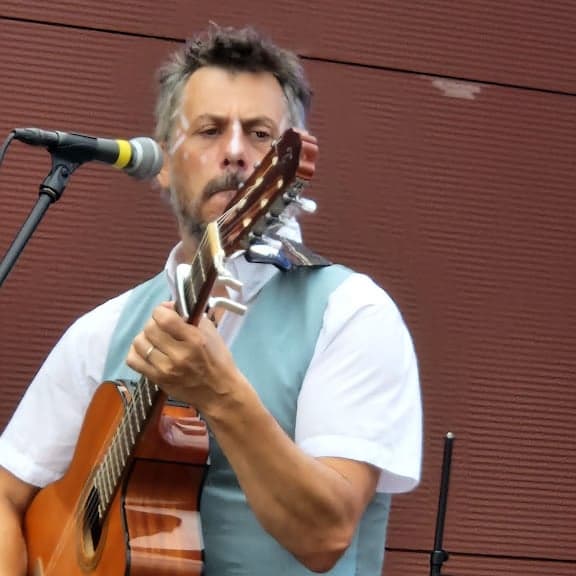 Homme avec peinture faciale blanche jouant de la guitare acoustique devant un microphone.